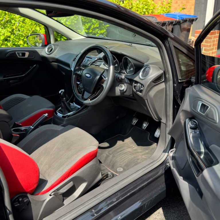 Interior of a car showcasing red and grey upholstery and dashboard controls.